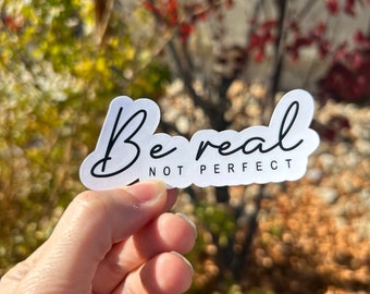 May include: A white die-cut sticker with a black script font reading Be real and a smaller black sans-serif font underneath reading NOT PERFECT. The sticker has a smooth, rounded edge contour that follows the shape of the lettering.