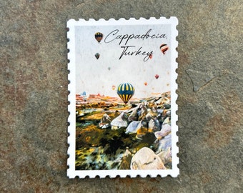 May include: A rectangular stamp featuring a landscape of Cappadocia, Turkey, with hot air balloons. The stamp has a white border with a perforated edge. The text "Cappadocia, Turkey" is written across the top.