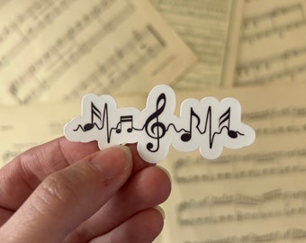 May include: A white sticker with a black musical note heartbeat design. The design includes a treble clef, musical notes, and a heartbeat line.