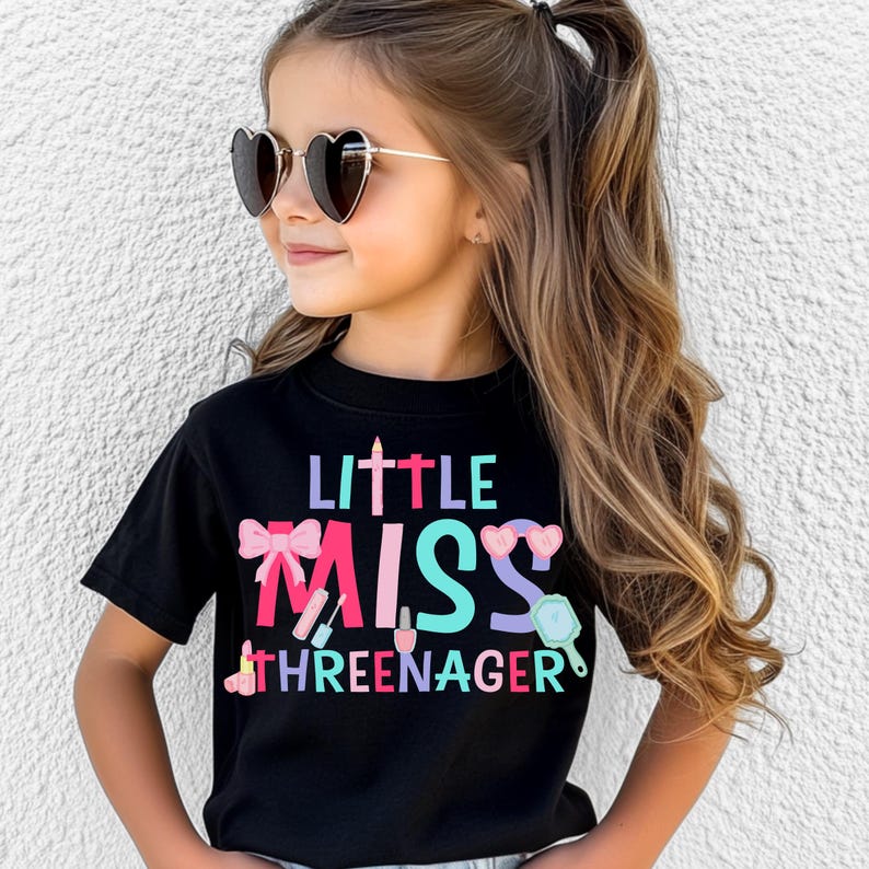 May include: A black t-shirt with the text "Little Miss Threenager" in colorful letters and a pink bow, lipstick, nail polish, and a mirror graphic.