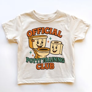 May include: Cream-colored toddler t-shirt with a retro design. The shirt features a smiling toilet and roll of toilet paper, with the words "OFFICIAL POTTY TRAINING CLUB" in orange and green.
