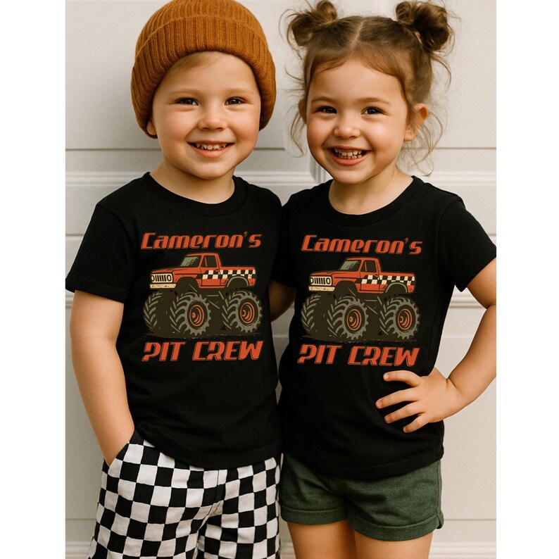 Pu&ograve; includere: Due bambini con magliette nere con una grafica di monster truck rosso e la scritta "Cameron's Pit Crew". Uno indossa un berretto marrone e pantaloncini a scacchi, l'altro pantaloncini verdi.