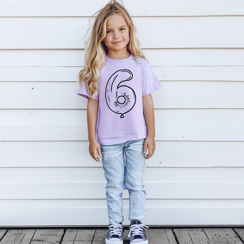 May include: A young person wearing a lavender t-shirt with a black outline of a number six balloon. The shirt is a birthday shirt for a six-year-old.