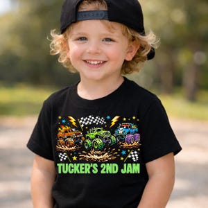 Może przedstawiać: Czarny t-shirt z trzema kolorowymi monster truckami, z szachownicami i błyskawicami. Tekst "TUCKER'S 2ND JAM" jest wydrukowany na zielono. Koszulka jest noszona przez uśmiechnięte dziecko.