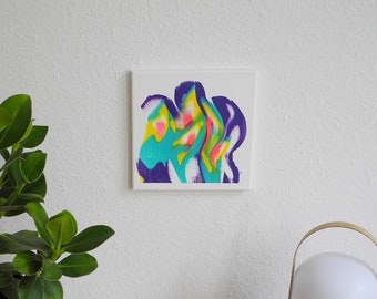 May include: A small abstract painting with swirls of purple, blue, green, yellow, and pink on a white background. The painting is hanging on a white wall above a wooden table.