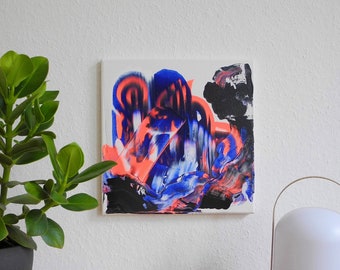 May include: Abstract painting on canvas with bold strokes of blue, pink, and black paint. The painting is displayed on a wall with a potted plant and a white lamp with a wooden base.