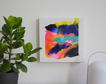 May include: Abstract painting with vibrant colors of pink, blue, yellow, and green on a white canvas. The painting is framed and hanging on a white wall.