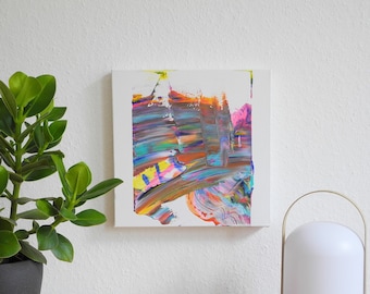 May include: Abstract painting with colorful brushstrokes in shades of blue, green, orange, pink, and yellow on a white canvas. The painting is framed and hanging on a white wall.