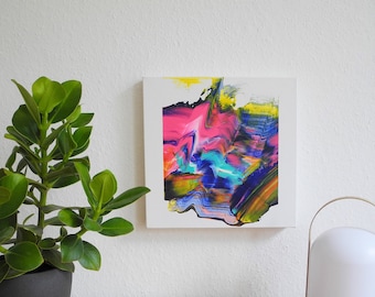 May include: Abstract painting with vibrant colors of pink, blue, green, and yellow on a white canvas. The painting is framed and hanging on a white wall.