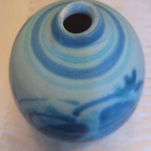 May include: A small, round ceramic vase with a narrow opening. The vase is painted with concentric blue and light blue swirls, and has a dark blue floral design. The vase is a decorative item.