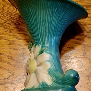 May include: A green glazed ceramic vase with a wide, flared opening and a floral design. The vase features a white flower with yellow center and green leaves.