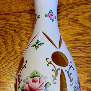 May include: A white glass vase with a gold rim and intricate cut-out design. The vase is decorated with hand-painted pink and blue flowers.