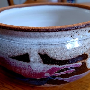 May include: A white ceramic bowl with a brown rim and abstract brown, pink, and blue designs. The bowl is glazed and has a glossy finish.