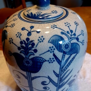 May include: A white ceramic jar with a blue lid and blue floral designs. The jar has a crackled glaze finish.