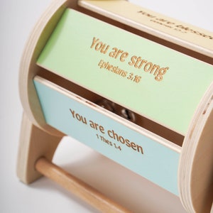 May include: Wooden toy with a handle that rotates to reveal three different inspirational messages: "You are strong, Ephesians 3:16", "You are chosen, 1 Thes 1:4", and "You are blessed, Romans 8:32".