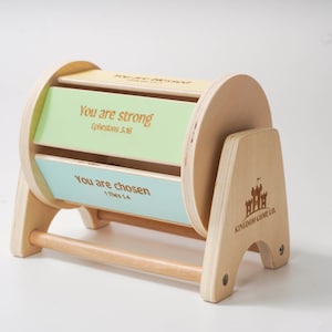 May include: Wooden toy with a spinning cylinder that has two inspirational messages: "You are strong, Ephesians 3:16" and "You are chosen, 1 Thessalonians 1:4". The toy is made by Kingdom Come Co.