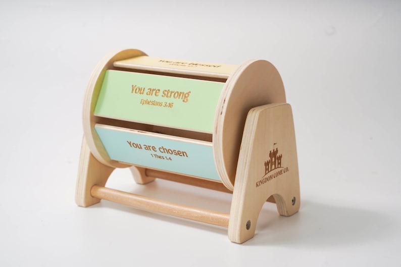 May include: Wooden toy with a spinning cylinder that has two inspirational messages: "You are strong, Ephesians 3:16" and "You are chosen, 1 Thessalonians 1:4". The toy is made by Kingdom Come Co.