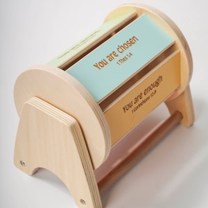 May include: Wooden box with a rotating cylinder that displays inspirational messages. The cylinder has two visible panels, one light blue with the text "You are chosen 1 Thess 1:4" and one orange with the text "You are enough 1 Corinthians 12:9".