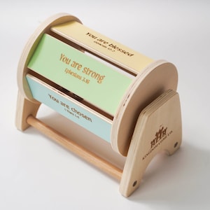 May include: A wooden toy with a spinning cylinder that has three colourful panels with inspirational messages and scripture references: "You are blessed", "You are strong", and "You are chosen". The toy is made by Kingdom Kids Co.