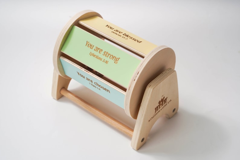 May include: A wooden toy with a spinning cylinder that has three colourful panels with inspirational messages and scripture references: "You are blessed", "You are strong", and "You are chosen". The toy is made by Kingdom Kids Co.