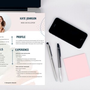 May include: A web developer's CV for Kate Johnson, with a photo, contact details, skills, and experience. The document is on a white surface with a laptop, a smartphone, pens, and a pink sticky note.