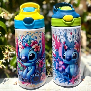 May include: Two water bottles with colorful designs. One has a yellow and blue lid, the other has a green and blue lid. Both bottles feature a blue cartoon character surrounded by flowers and splashes of color. The bottles are white with a glossy finish.