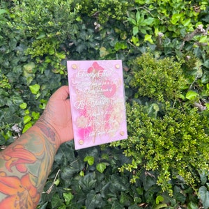 May include: A pink and gold acrylic invitation with a floral design and the text "Twenty Three" and "Please join us for a Tea Party in honour of La'Charte Curtis August 17, 2022 at 7:00 PM The Gage Room"