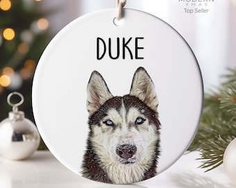 May include: White ceramic Christmas ornament with a husky dog illustration and the name "DUKE" printed in black.
