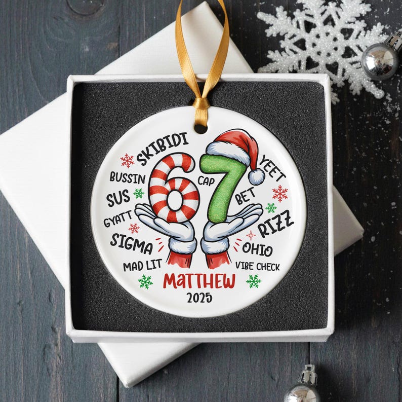 May include: A white ceramic Christmas ornament with a gold ribbon, presented in a gift box. The ornament features the number "67" in a candy cane design and green with a Santa hat. Text includes "SKIBIDI", "Matthew", and "2025".