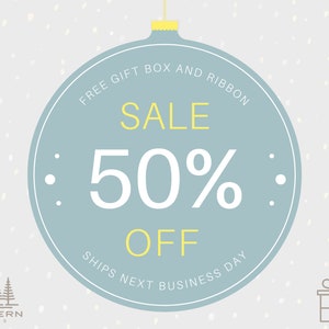 May include: A light blue Christmas ornament design with the text "SALE 50% OFF". The ornament also includes the text "FREE GIFT BOX AND RIBBON" and "SHIPS NEXT BUSINESS DAY". The background is light gray with white dots.