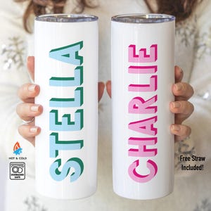 May include: Two white cylindrical tumblers with metal lids. The left tumbler features the name STELLA in a 3D block font with teal and light blue colors. The right tumbler features the name CHARLIE in a 3D block font with pink and magenta colors.