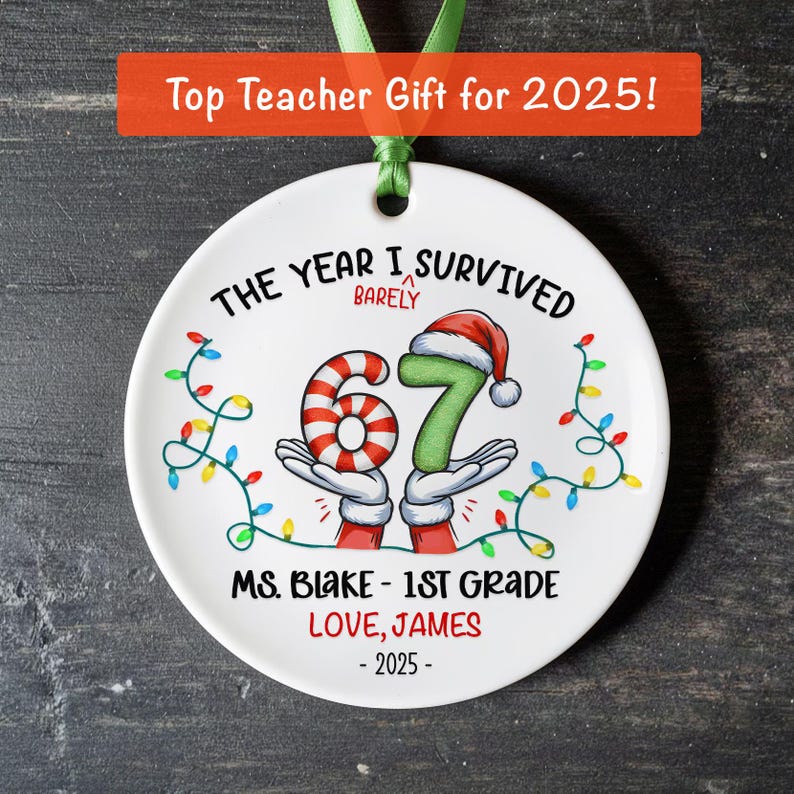 May include: A white ceramic ornament with a green ribbon for hanging. The ornament features the text "THE YEAR I SURVIVED BARELY" and the numbers "67" in a festive design, with the text "MS. BLAKE - 1ST GRADE LOVE, JAMES - 2025".