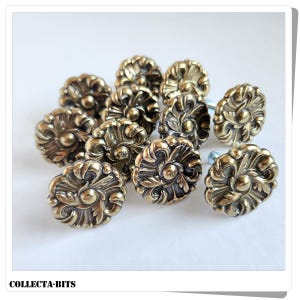 Può includere: Un gruppo di pomelli per mobili in ottone in stile antico con un design floreale ornato. I pomelli sono disposti su una superficie bianca, mettendo in risalto la loro lavorazione dettagliata e la finitura invecchiata. Il testo "COLLECTA-BITS" è in basso.