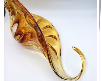 May include: A large amber glass bowl with a swirling design. The bowl is shaped like a flower with a long, curved stem.