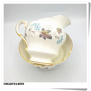 Può includere: Un set di brocca per la panna e zuccheriera bianca con un motivo floreale in tonalità di blu, rosa e verde. Il set ha un bordo dorato.