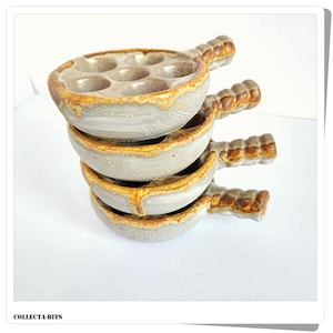 May include: A stack of four ceramic escargot dishes. Each dish is light gray with a brown rim and handle. The dishes have six circular indentations for holding snails. The handles are textured and brown. The dishes are stacked on top of each other.