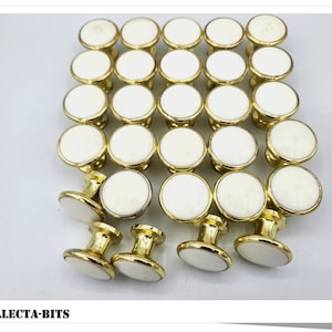 May include: A collection of 25 gold and white cabinet knobs. The knobs are round with a white centre and a gold rim. The knobs have a simple design and are perfect for adding a touch of elegance to any room.