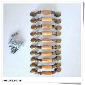 May include: Ten cabinet pulls with light wood central sections and antique brass ends. The pulls are arranged in a row, with a small bag of screws to the left. The text "COLLECTA-BITS" is at the bottom.