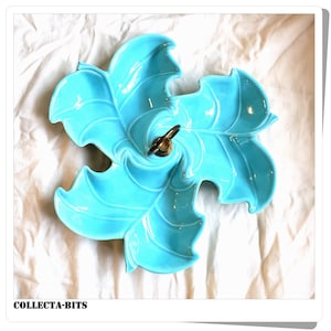 May include: A turquoise blue ceramic serving dish shaped like a stylised leaf with a gold metal handle in the centre. The dish has five sections and is perfect for serving snacks or appetizers.