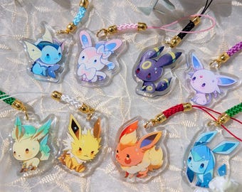 May include: A selection of clear acrylic charms depicting cartoon creatures in bright colours. Each charm has a colourful cord and gold-coloured clasp. The charms are presented on a white, textured surface.