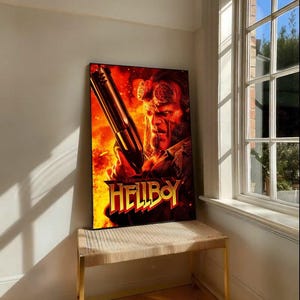 Puede incluir: Un póster enmarcado de la película Hellboy que muestra al personaje sosteniendo un arma grande contra un fondo de fuego. El título del póster, "HELLBOY", está en letras amarillas y rojas en negrita. El póster se muestra en un pequeño banco con una parte superior tejida.