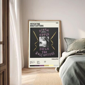 May include: A framed poster featuring the album art for Fiona Apple's "Fetch the Bolt Cutters." The poster has a black background with the album title and artist's name in a stylized font. A black and white image of a person is in the center.