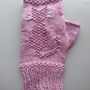 May include: A pink knitted fingerless glove with a white embroidered cat design.