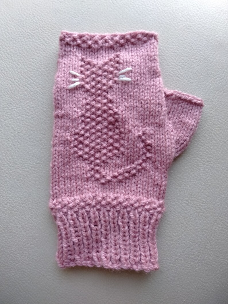 May include: A pink knitted fingerless glove with a white embroidered cat design.