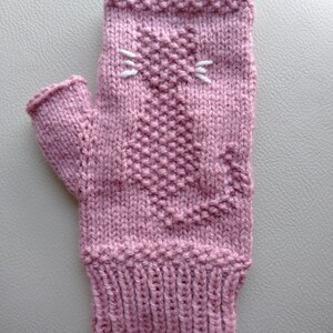 May include: A pink knitted fingerless glove with a white embroidered cat face.