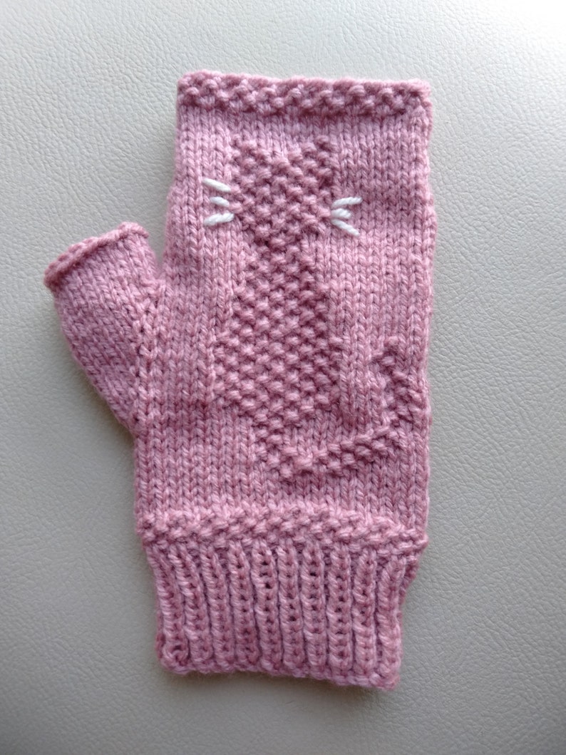 May include: A pink knitted fingerless glove with a white embroidered cat face.