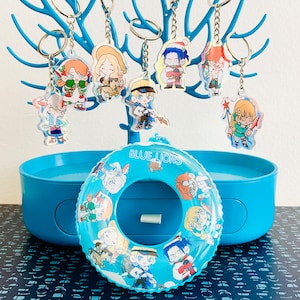 Könnte beinhalten: Ein blauer und weißer aufblasbarer Pool-Schwimmring mit dem Aufdruck "Blue Lions". Der Schwimmring ist von einer Vielzahl bunter Schlüsselanhänger mit Comicfiguren umgeben.