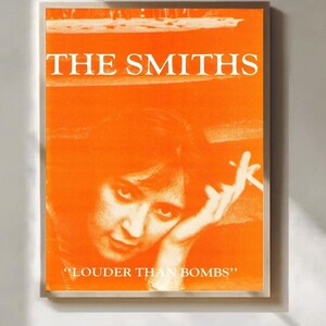 Könnte beinhalten: Orangefarbenes Poster mit dem Bandnamen "THE SMITHS" in weißen Großbuchstaben. Darunter ein Porträt einer Person mit Zigarette und dem Text "LOUDER THAN BOMBS".