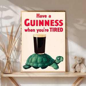 May include: A framed print featuring a pint of Guinness atop a green turtle, with the text "Have a GUINNESS when you're TIRED" in red. The artwork has a vintage, cartoon-like style, perfect for a pub or home bar.