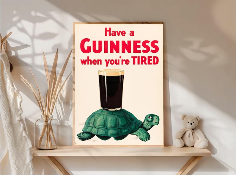 May include: A framed print featuring a pint of Guinness atop a green turtle, with the text "Have a GUINNESS when you're TIRED" in red. The artwork has a vintage, cartoon-like style, perfect for a pub or home bar.